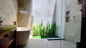 A modern bathroom with a freestanding bathtub, a wooden bench, a glass shower enclosure, and a small green plant area.