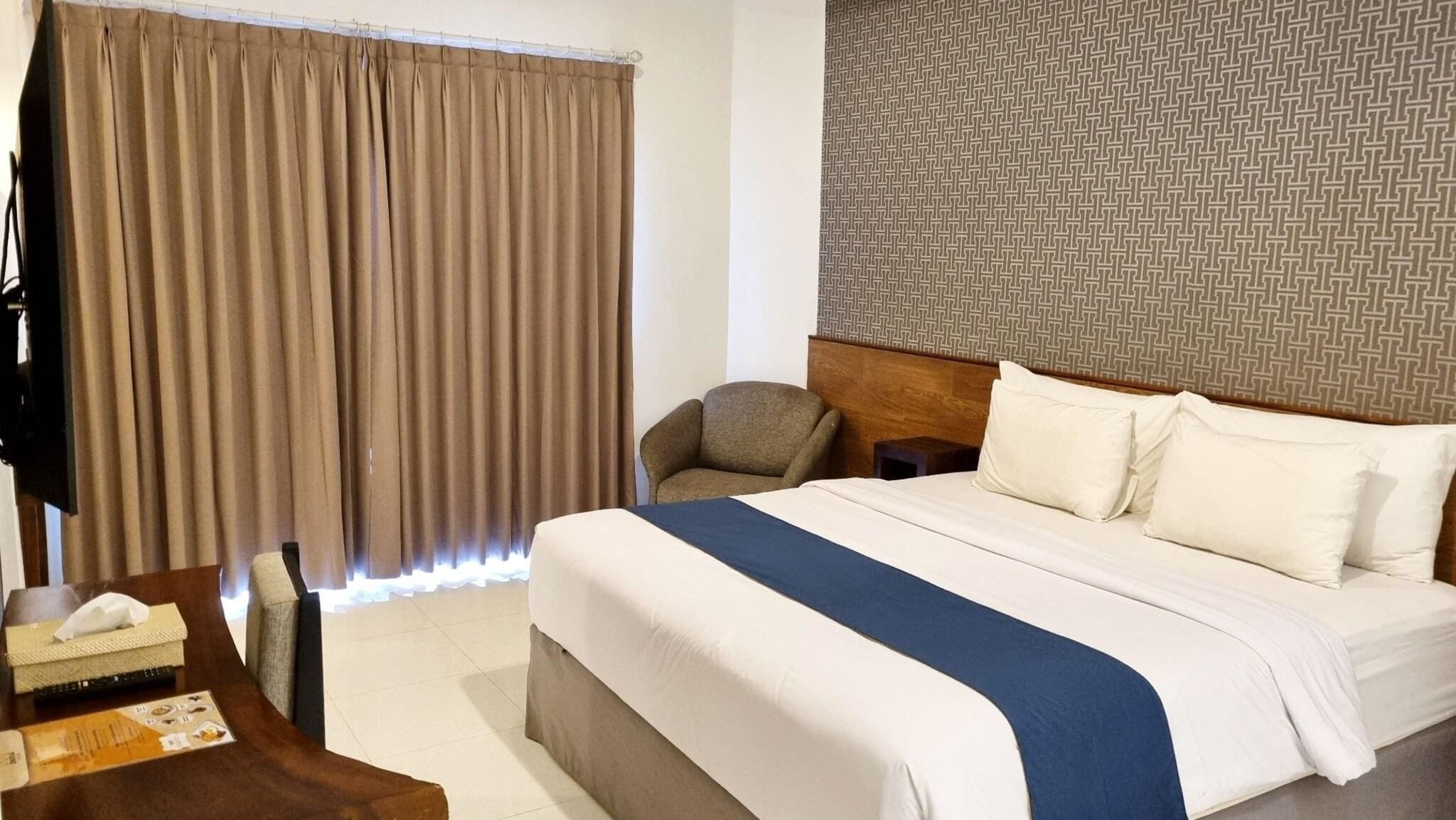 A hotel room with a bed, a chair, a desk with a tissue box, and a patterned wall.