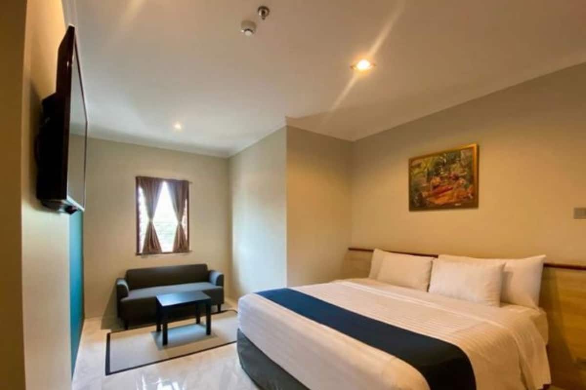 A hotel room with a bed, a sofa, a TV, and a painting on the wall.