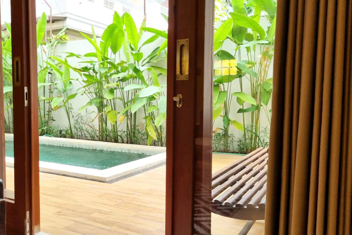 A view through an open door to a pool area with a wooden deck and lush greenery.