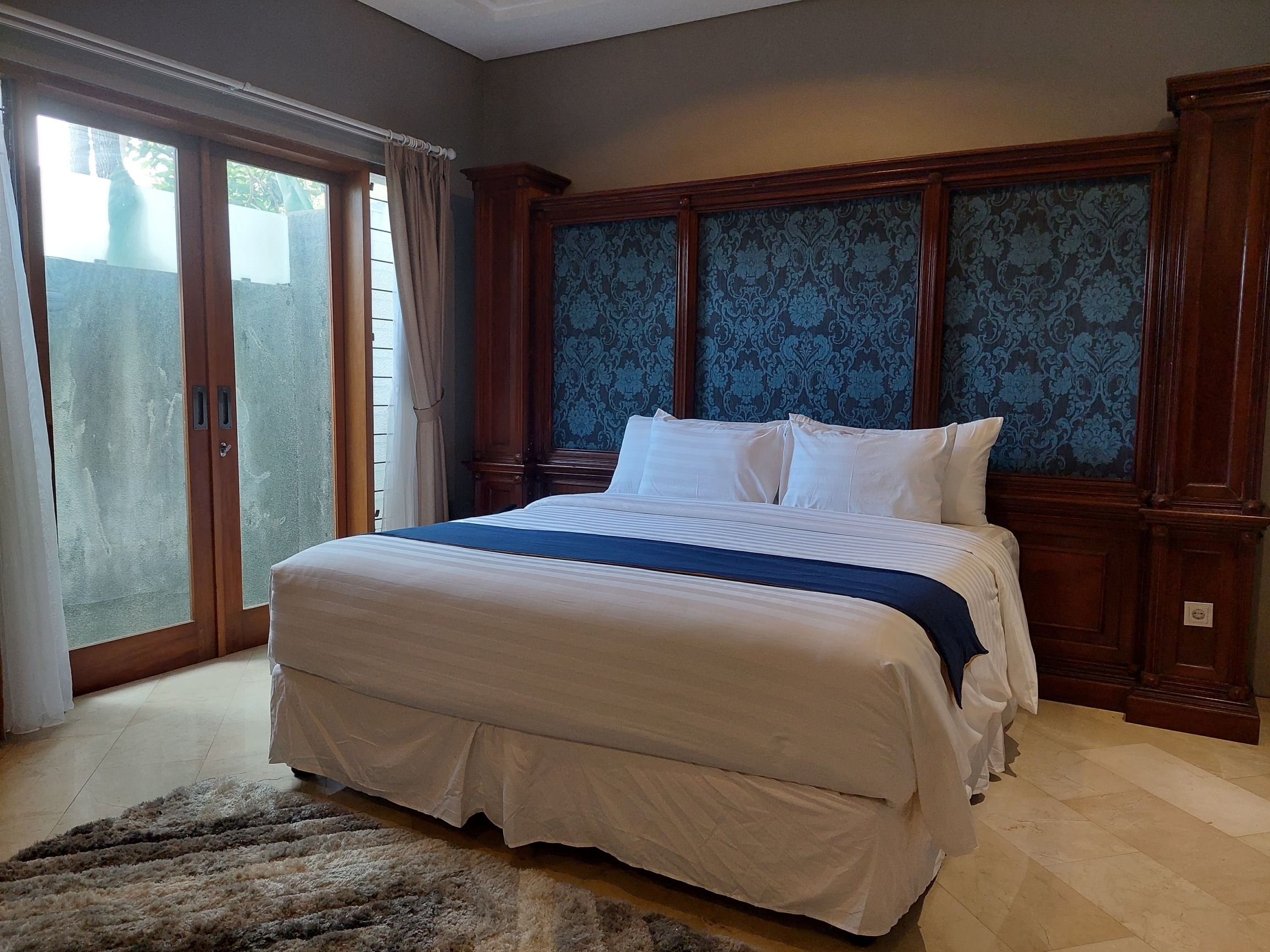 A bedroom with a large bed, wooden headboard, and a view through a sliding glass door.