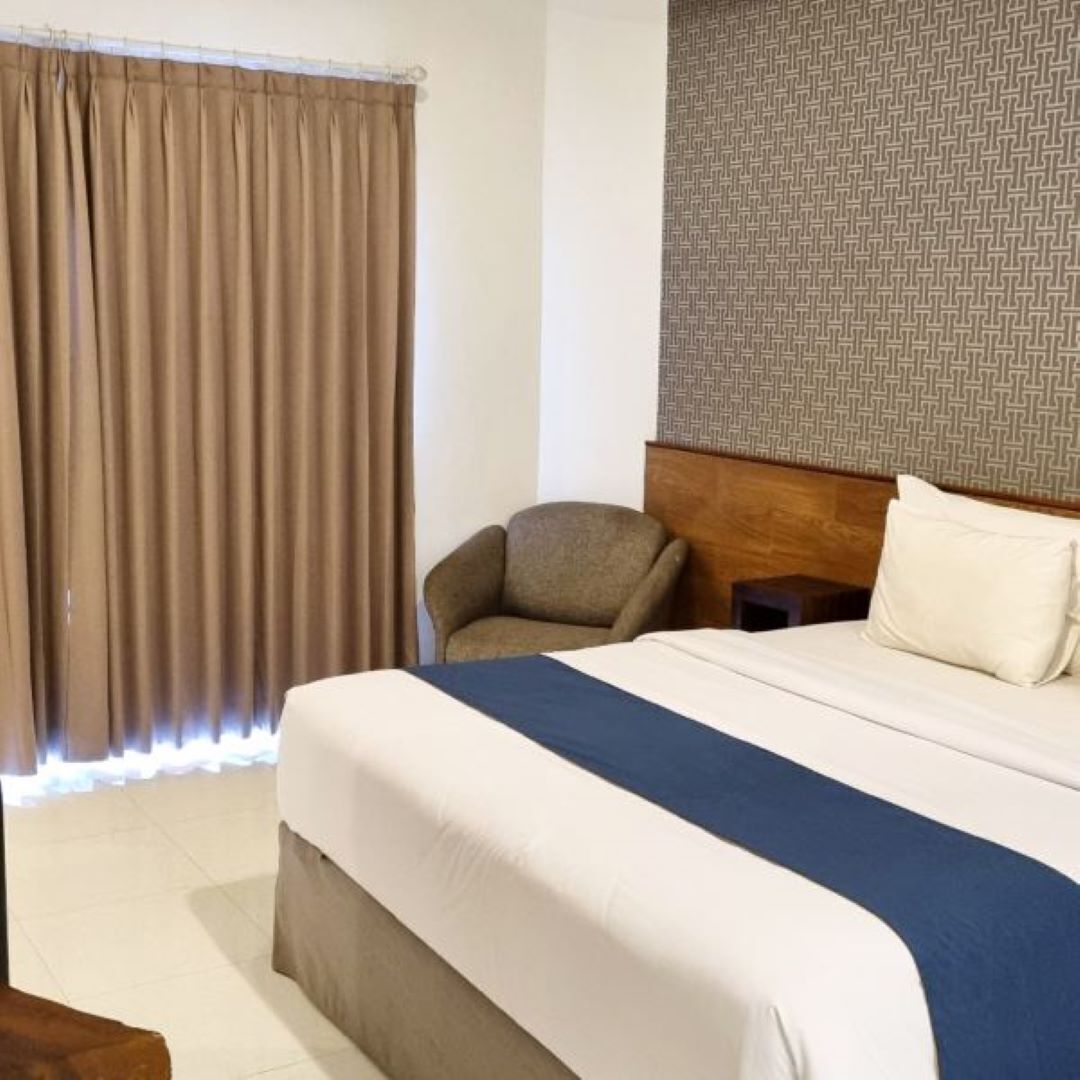 A hotel room with a bed, a chair, a nightstand, and a patterned wall.