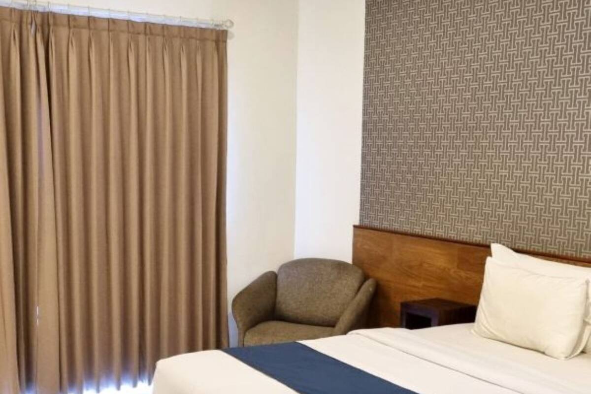 Ein Hotelzimmer mit Bett, Stuhl, Nachttisch und einer Wand mit Muster.