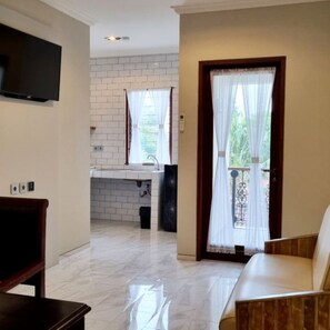 A room with a TV, a sofa, a kitchen area, and a window with curtains.
