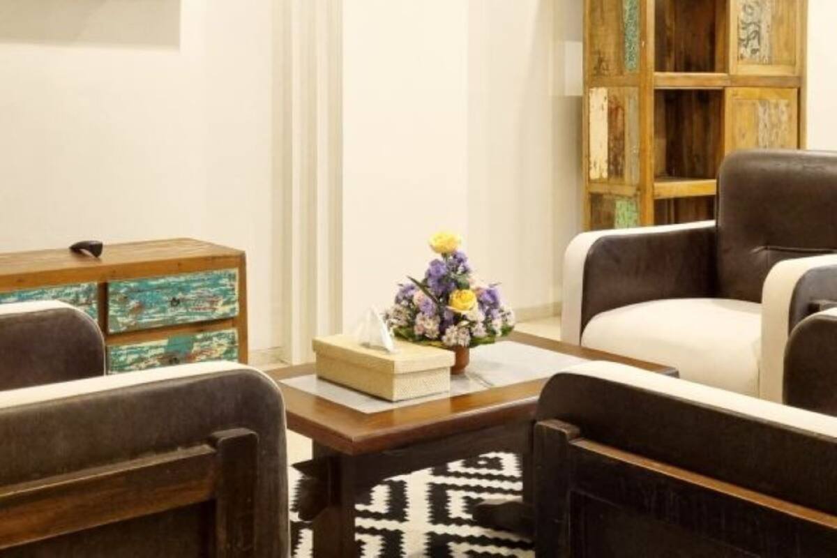 Ein Wohnzimmer mit Fernseher, einer Holzbibliothek, zwei Sesseln, einem Couchtisch und einem gemusterten Teppich.