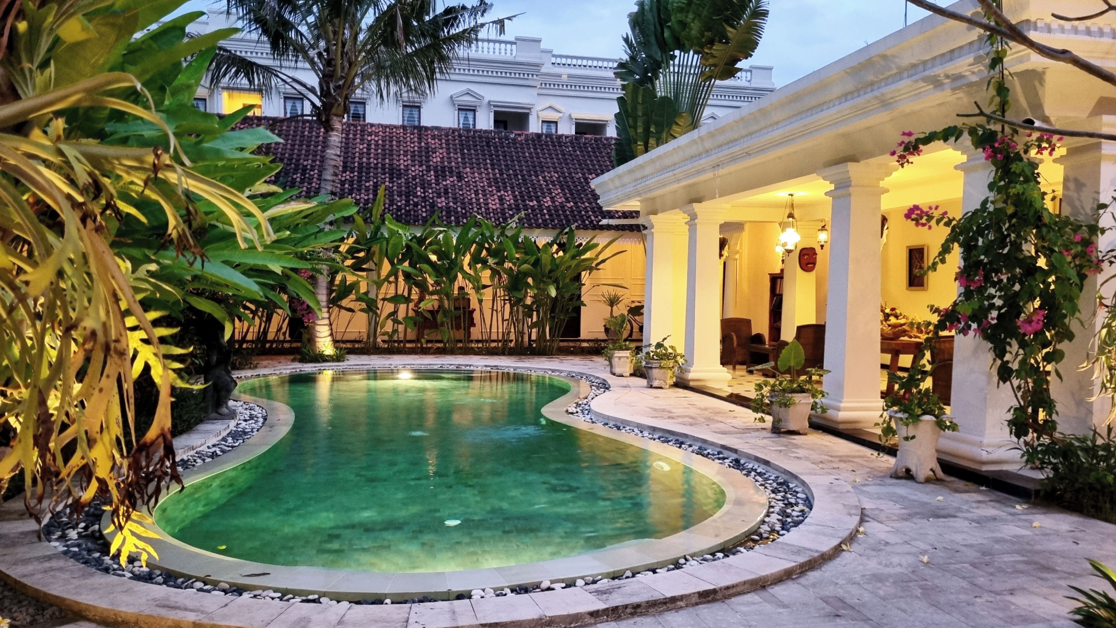 A swimming pool with a curved edge, surrounded by a stone border, and a covered seating area with columns.