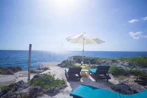 A beachside lounge with a white umbrella, lounge chairs, and a view of the ocean. - Sea Breeze Studio (Negril)