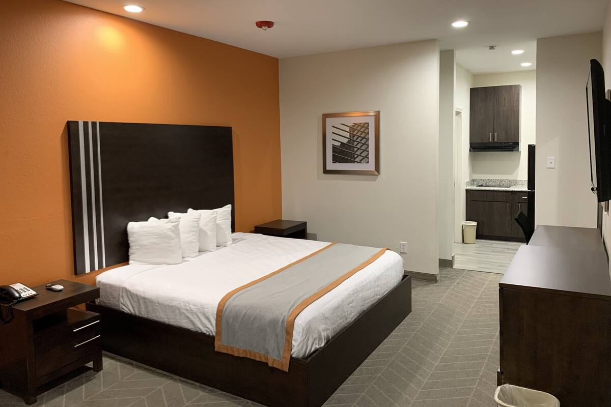 Quarto de hotel com cama, mesa de cabeceira e pequena escrivaninha com cadeira.