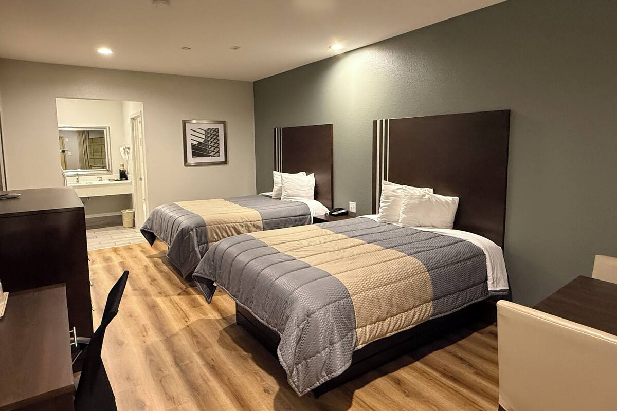 Quarto de hotel com duas camas, uma escrivaninha e um espelho.