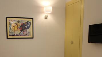 Une pièce avec un tableau abstrait encadré, un luminaire fixé au mur, une porte jaune fermée et un téléviseur à écran plat.
