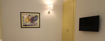 Una habitación con un cuadro abstracto enmarcado, una lámpara de pared, una puerta amarilla cerrada y un televisor de pantalla plana.