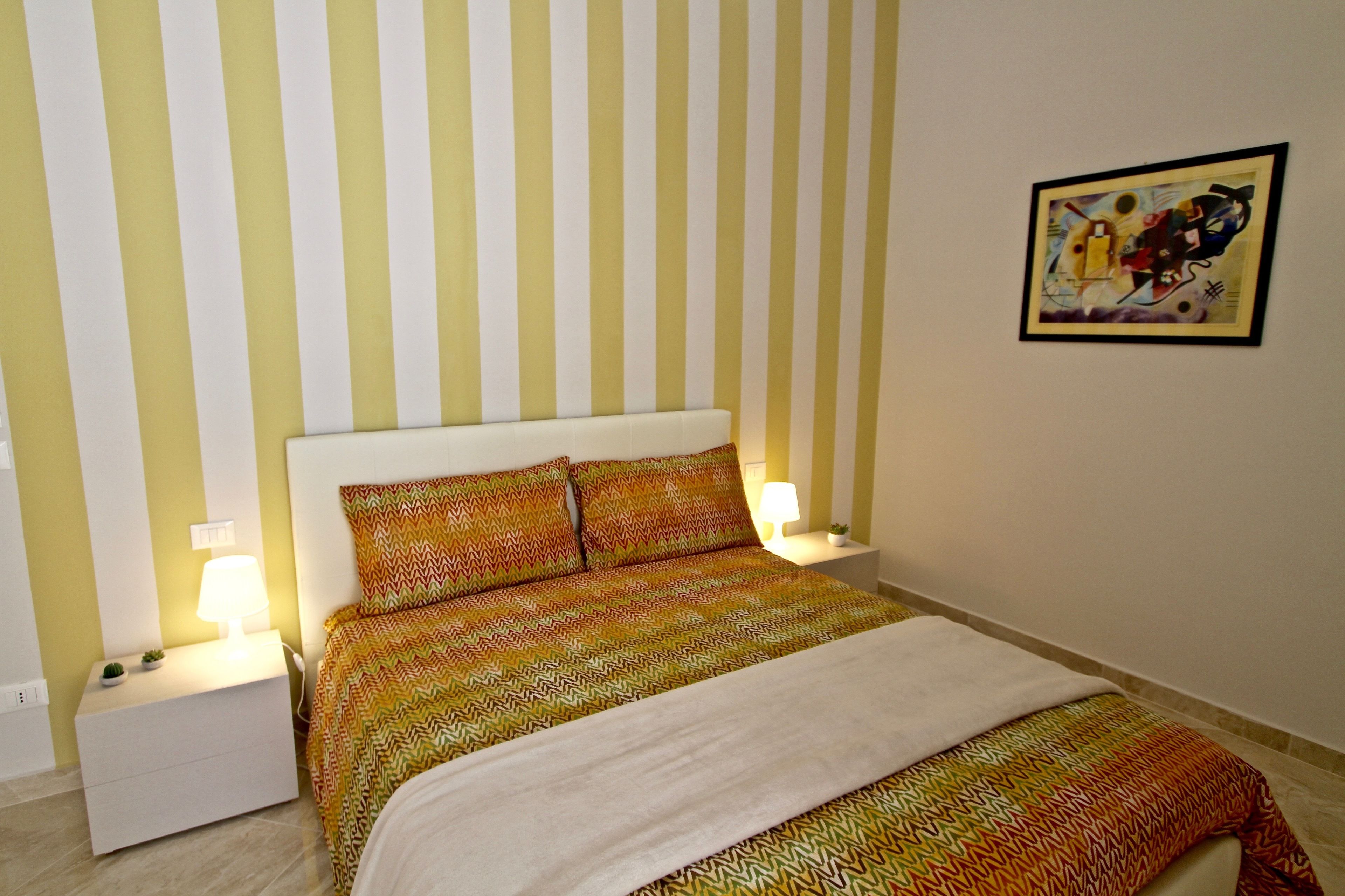 Un dormitorio con pared a rayas, una cama con ropa de cama estampada, dos lámparas de noche y una obra de arte enmarcada en la pared.