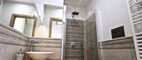 A modern bathroom with a large mirror, a vessel sink, a shower enclosure, and a towel rack.