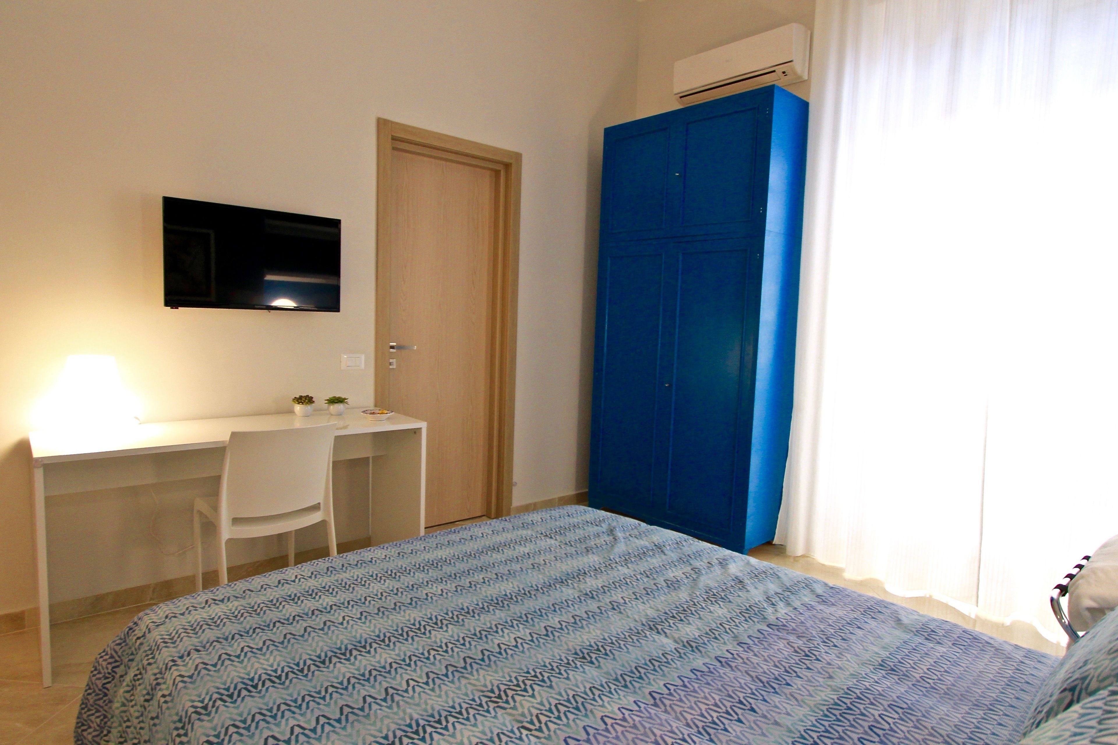 Un dormitorio con cama, escritorio y silla, televisión montada en la pared y armario.