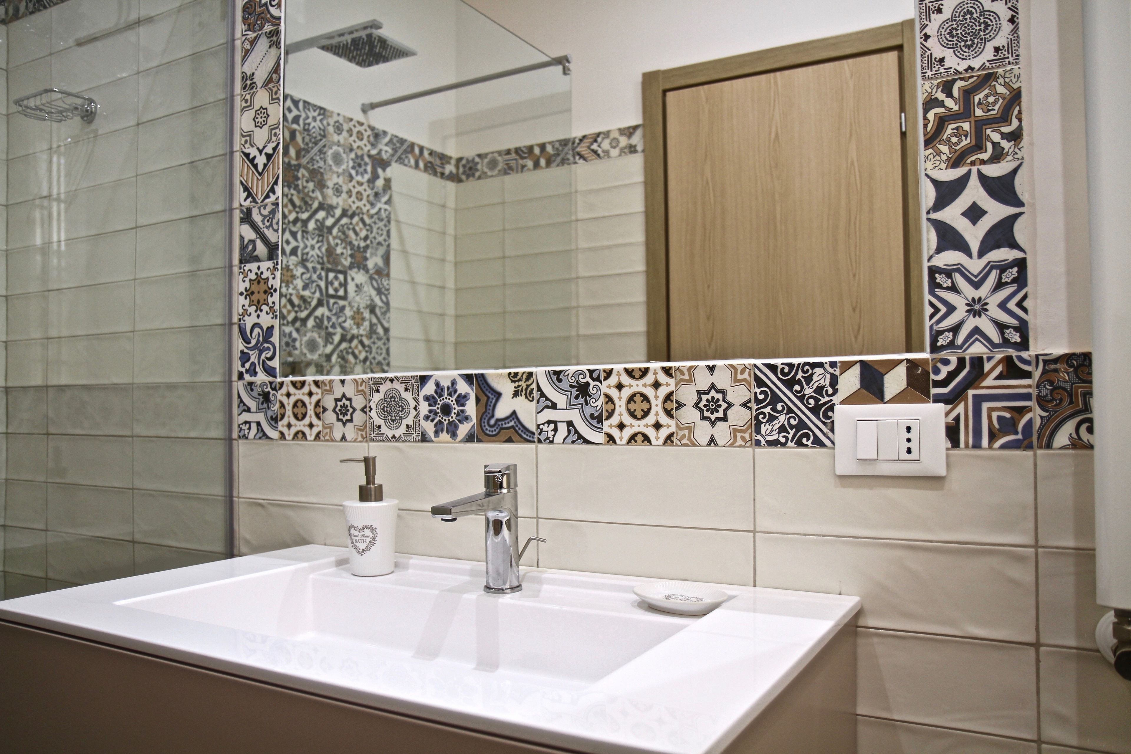 Une salle de bain avec un lavabo blanc, un robinet moderne et un miroir. Les murs sont recouverts de carreaux aux motifs décoratifs.