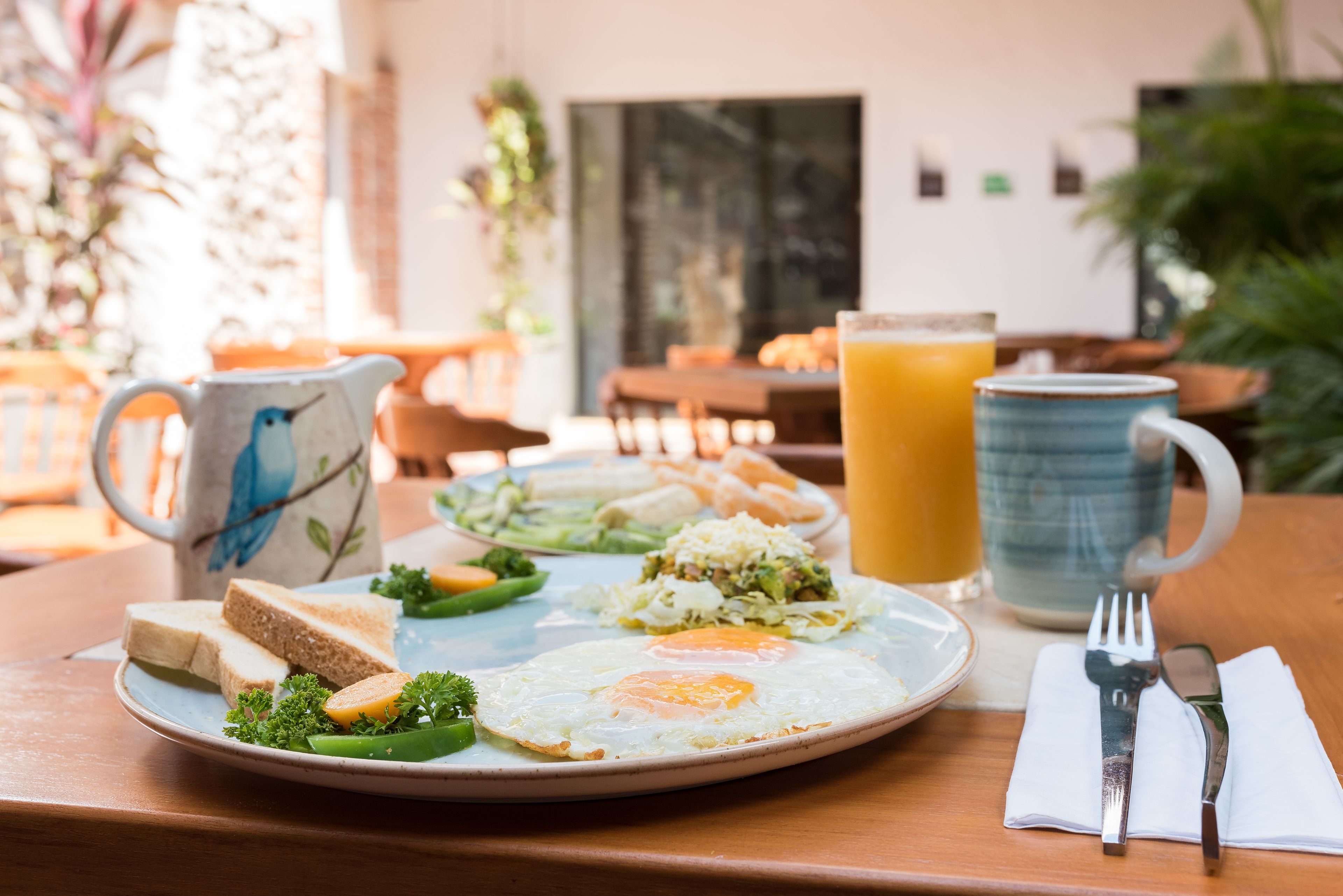 A breakfast plate with toast, eggs, and vegetables, a pitcher of orange juice, and a mug with a bird design.