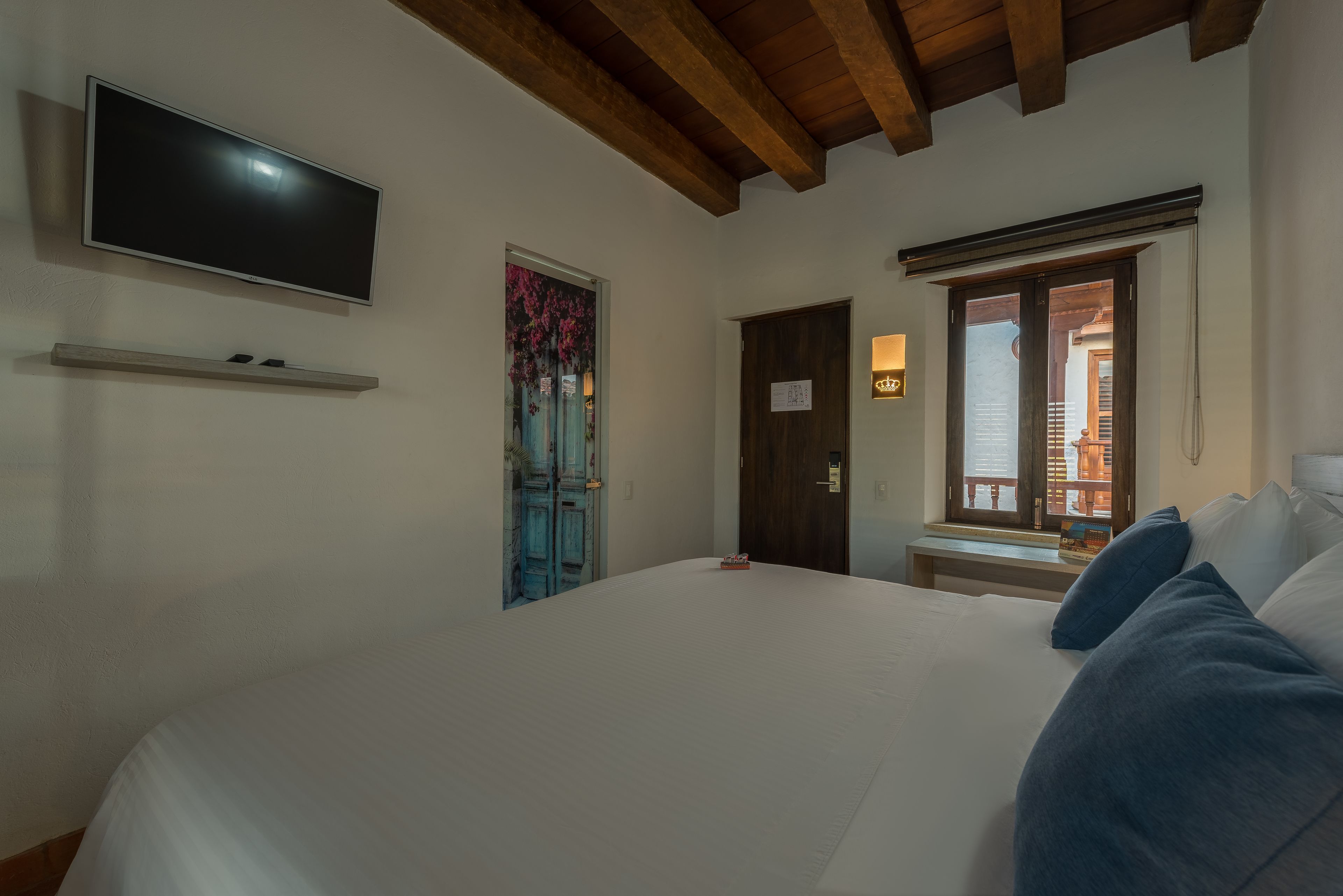 Une chambre à coucher avec un lit, un téléviseur fixé au mur, une porte avec une fenêtre et un banc près de la fenêtre.