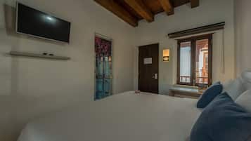 Une chambre à coucher avec un lit, un téléviseur fixé au mur, une porte avec une fenêtre et un banc près de la fenêtre.