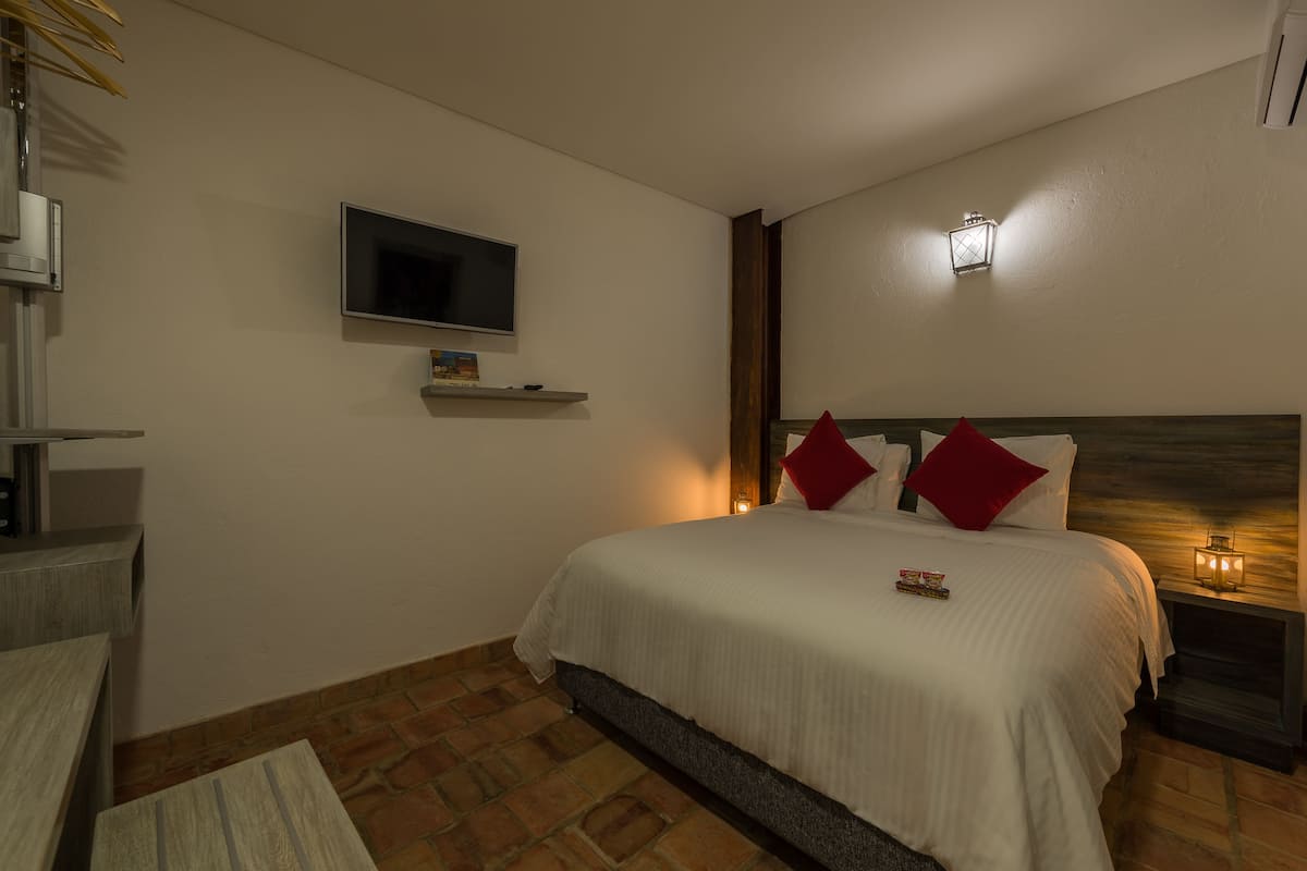Une chambre à coucher avec un lit, un téléviseur fixé au mur et une table de chevet avec une lampe.