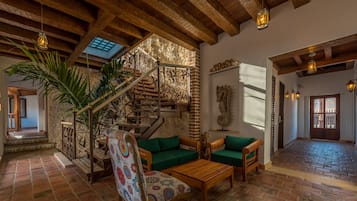 Uma sala de estar ampla com escada de madeira, sofás verdes, uma poltrona estampada e piso ladrilhado.
