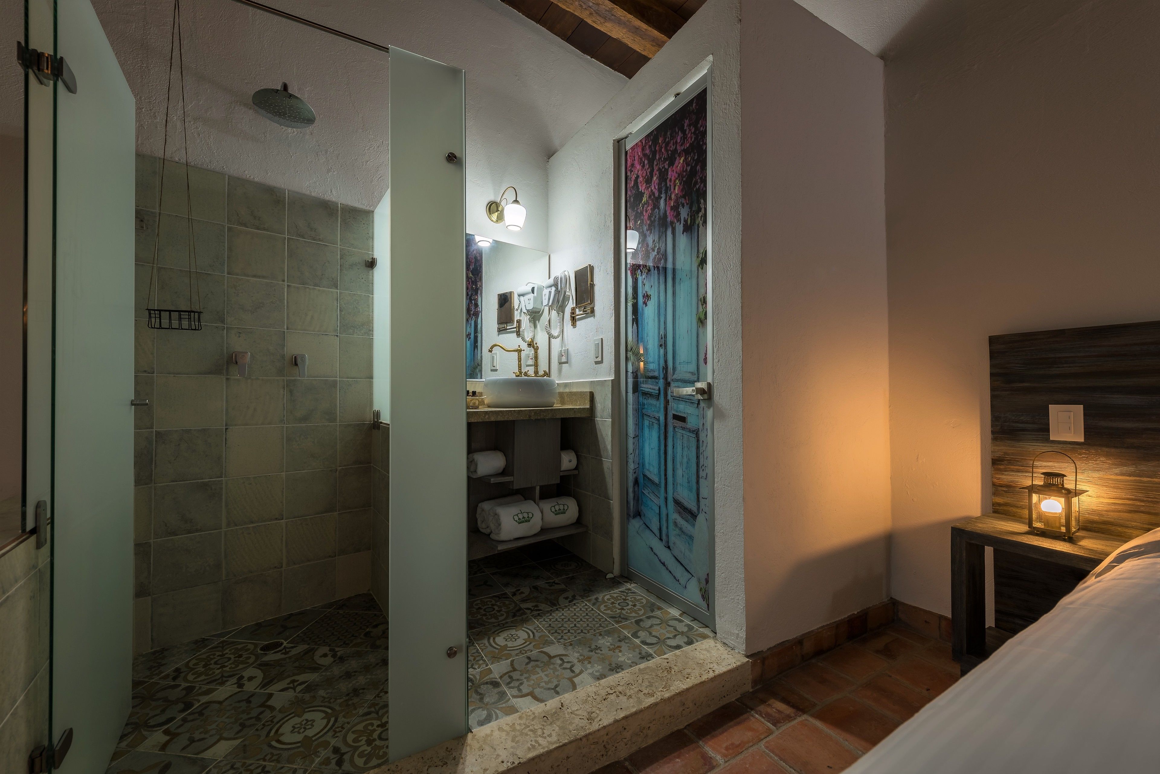 A bathroom with a shower, a sink with a mirror, and a door with a floral curtain.