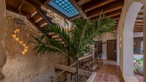 Un escalier avec une rampe en fer forgé, un mur en pierre et un luminaire suspendu.