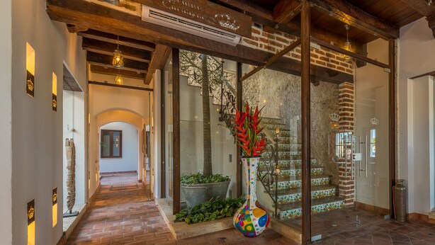 Un hall d’hôtel avec un sol en briques, un vase coloré rempli de fleurs rouges et un escalier doté d’une rampe en verre.
