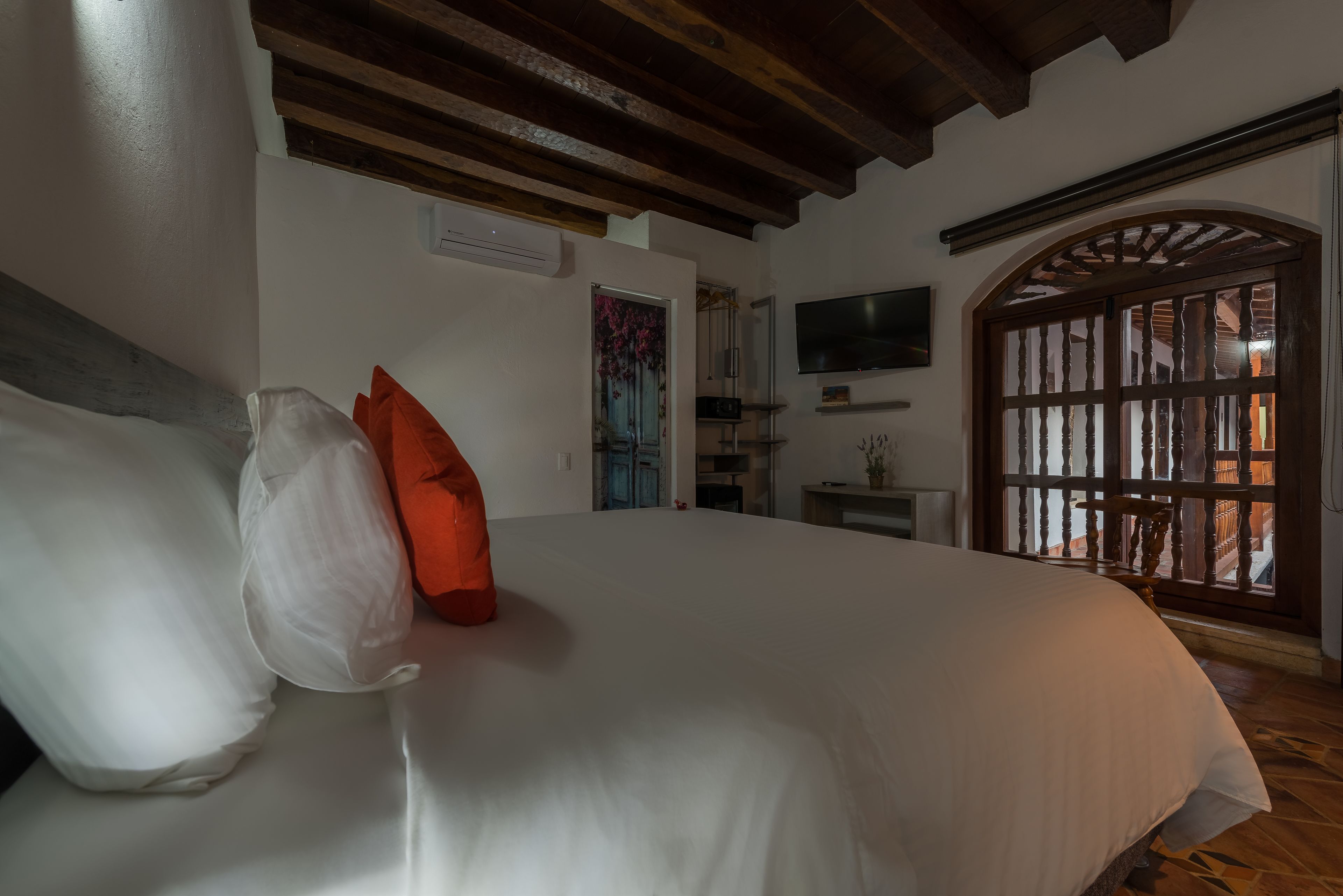 Un dormitorio con cama, almohadas, televisor, ventana con vistas y techo de madera.