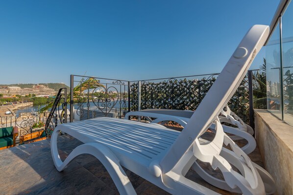 A white lounge chair on a balcony with a clear view of a body of water and distant buildings.