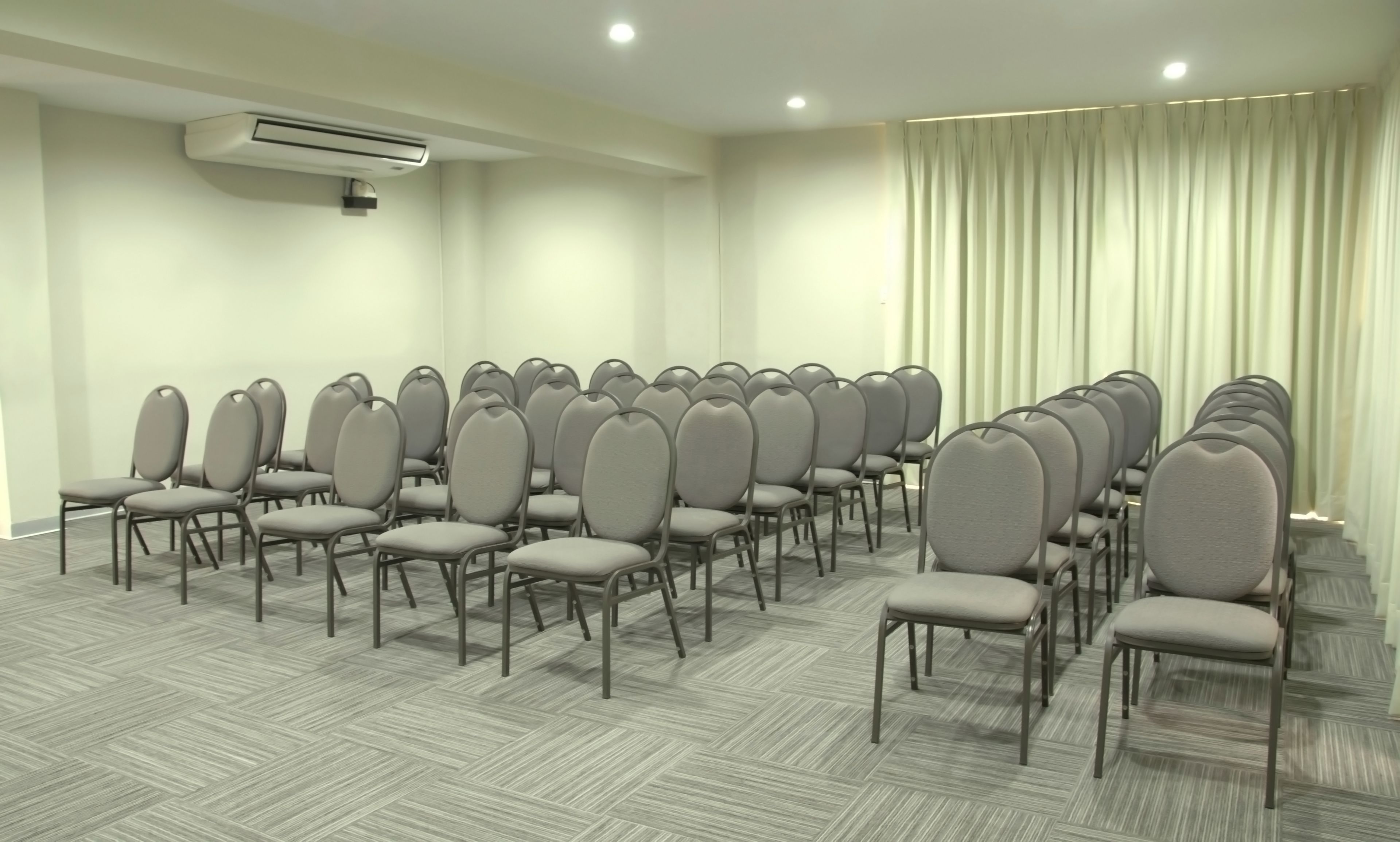 A conference room with rows of chairs, an air conditioning unit, and a large window with curtains.