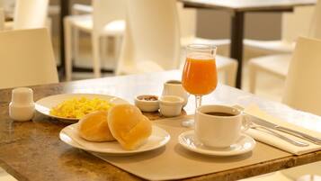 Una escena de desayuno con huevos, panes, café y zumo de naranja sobre una mesa.