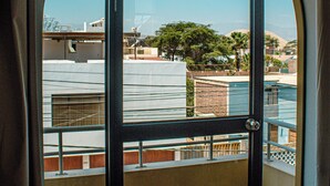 A room with a large arched window, a bed with a patterned bedspread, and a view of buildings and trees outside. - Del Valle House (Ica)