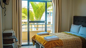A hotel room with a bed, a desk, a chair, and a balcony with a view of palm trees. - Del Valle House (Ica)