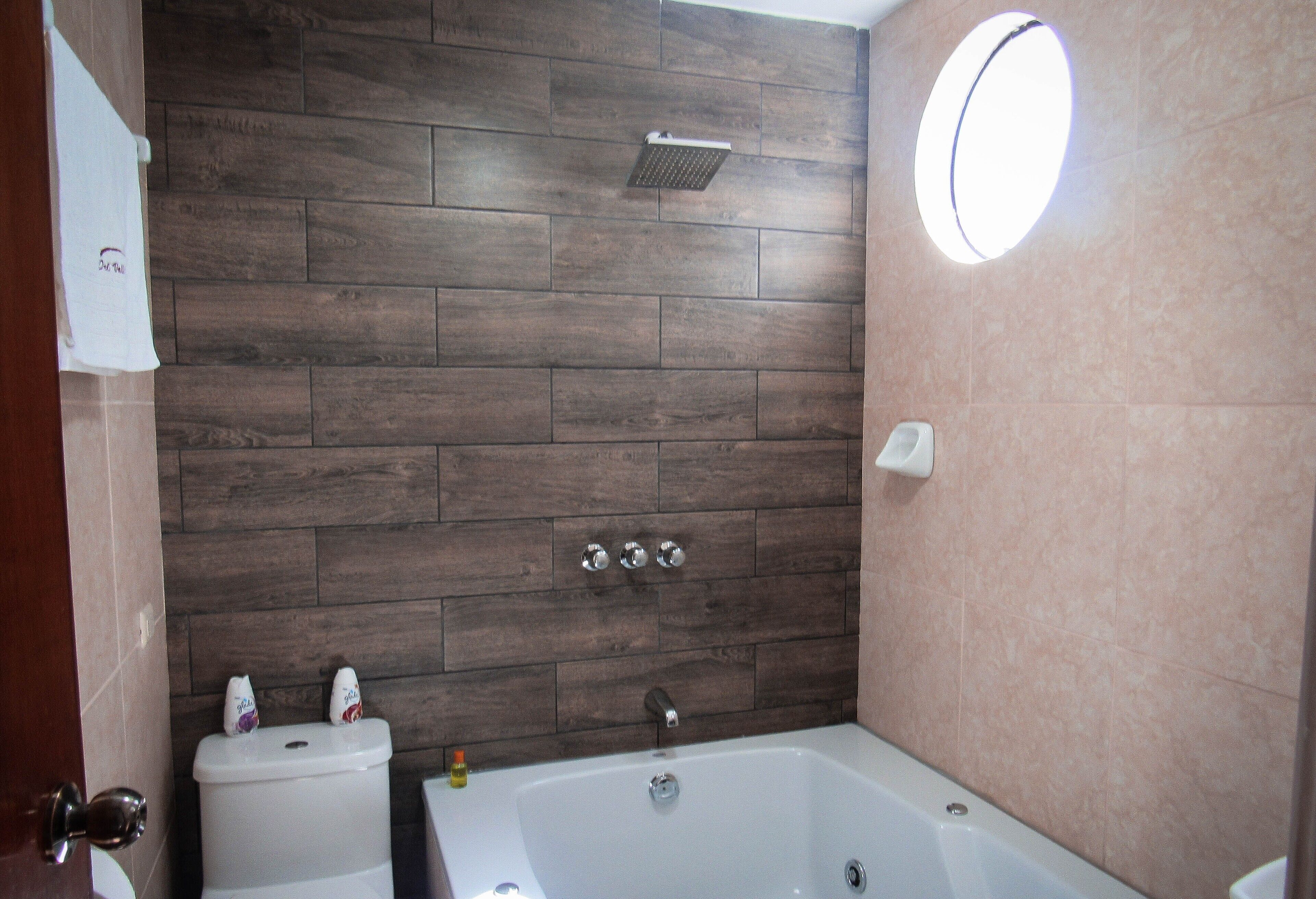 A bathroom with a wooden wall, a toilet, a bathtub, and a round mirror.
