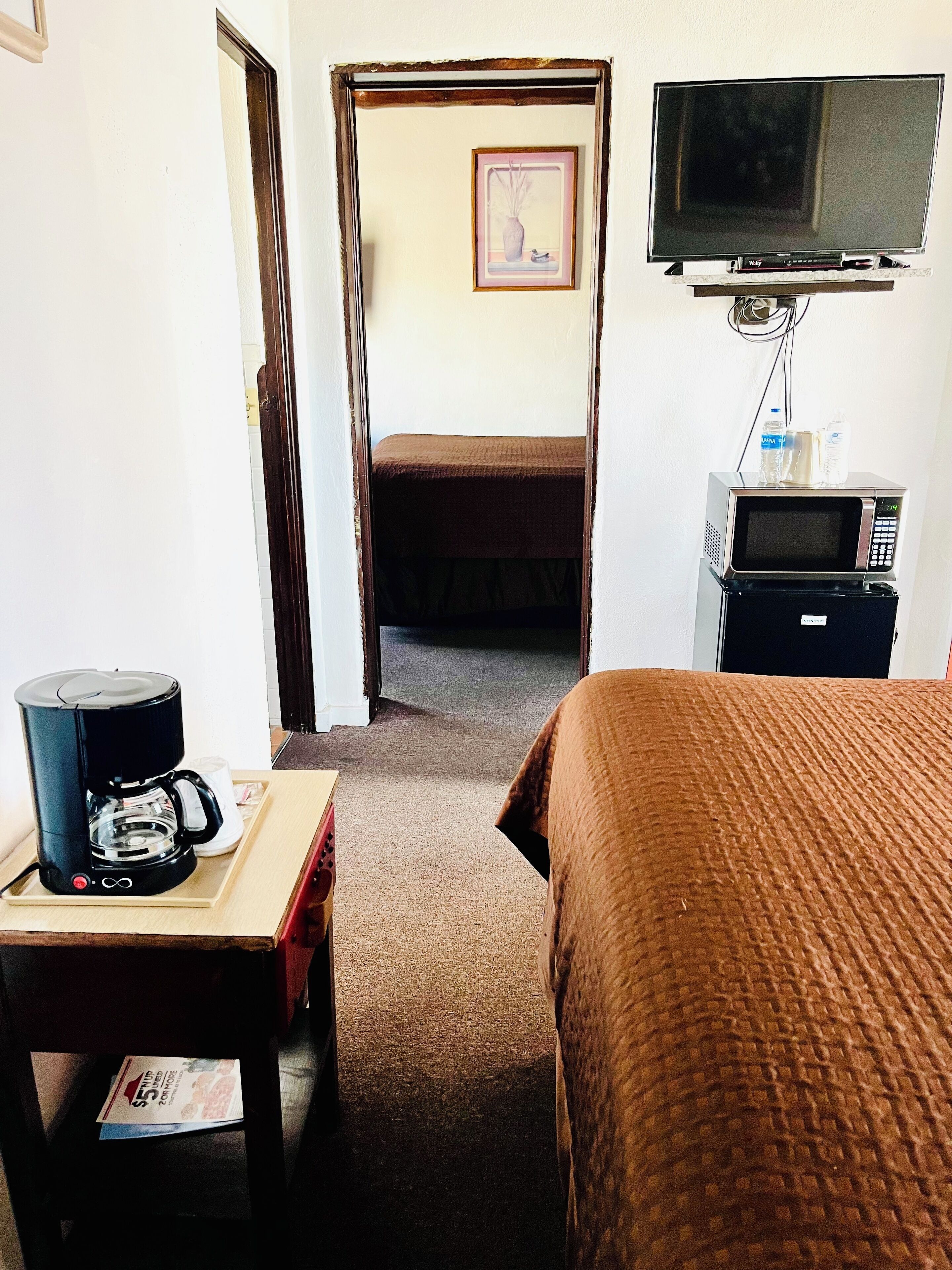 A hotel room with a bed, a coffee maker, a microwave, and a television.