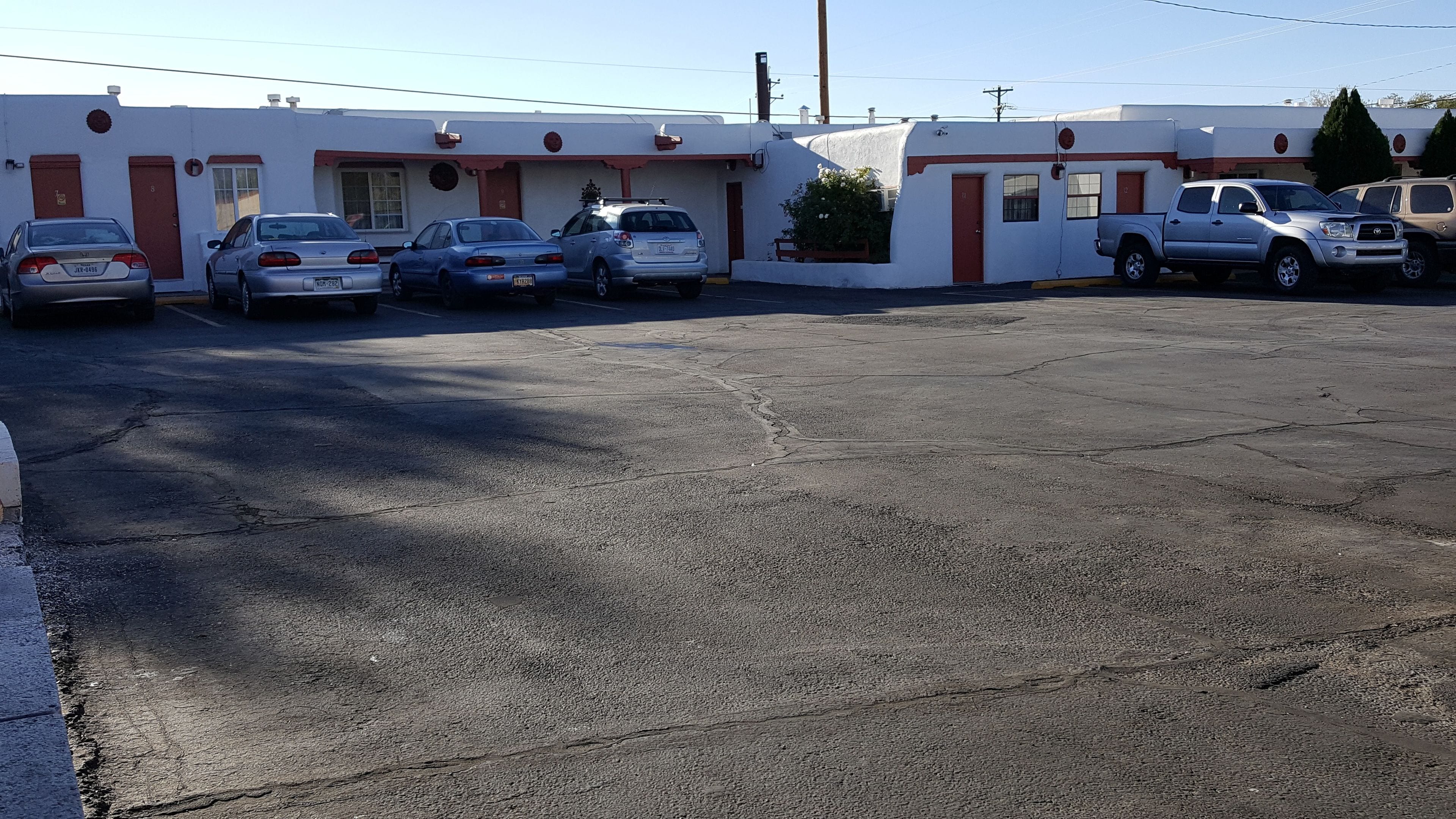 A parking lot with several cars parked in front of a building with red doors and white walls.