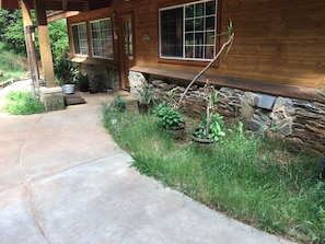 Une maison en bois avec des fondations en pierre, un chemin en béton et des plantes en pot.