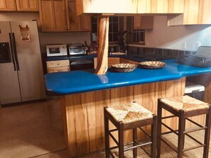 A kitchen with wooden cabinets, a blue countertop, a built-in island with stools, and a refrigerator.