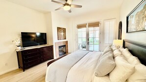 Un dormitorio con una cama, un televisor sobre una cómoda, una chimenea y un ventilador de techo.