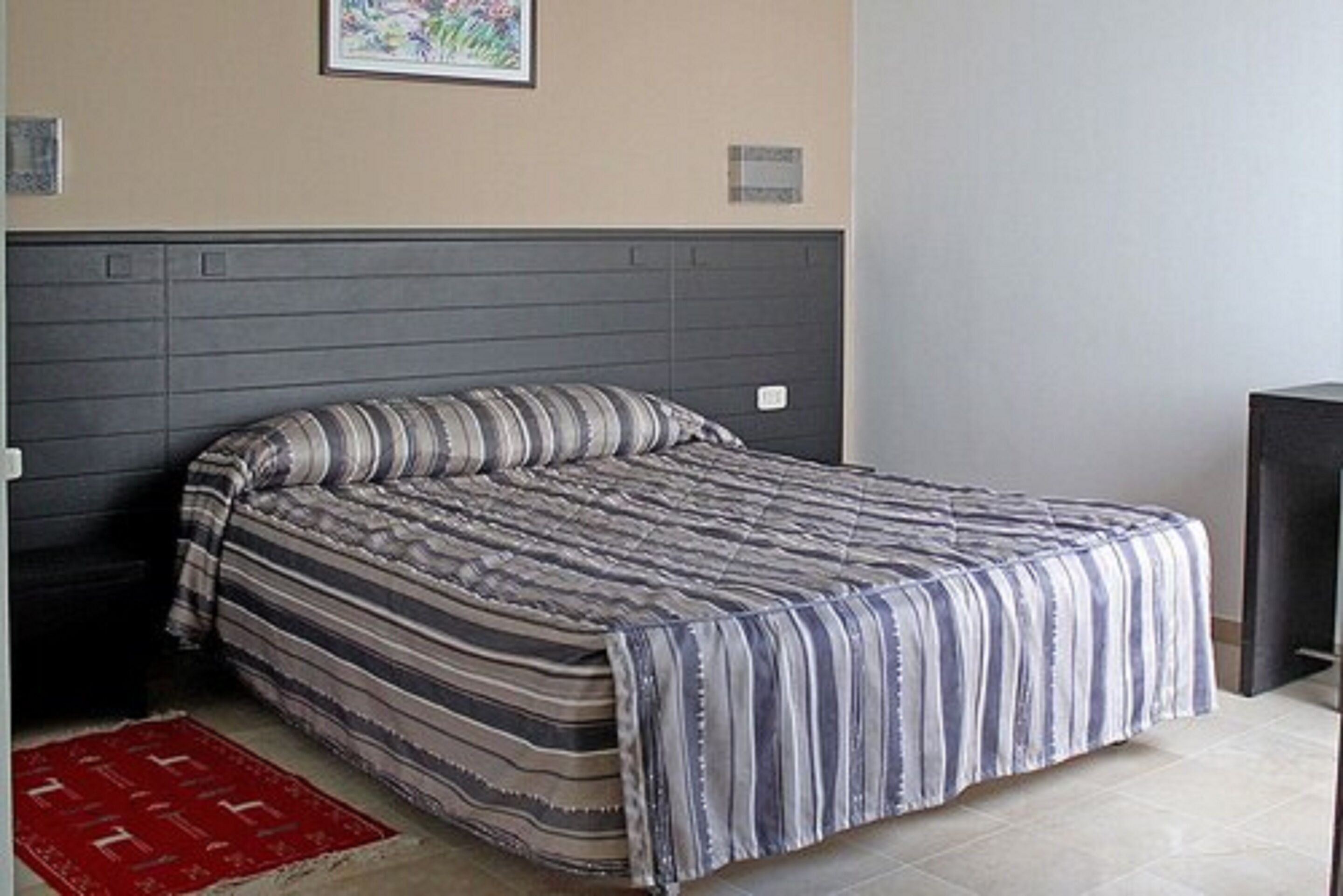 A bed with a striped bedspread, a headboard, and a red rug on the floor.