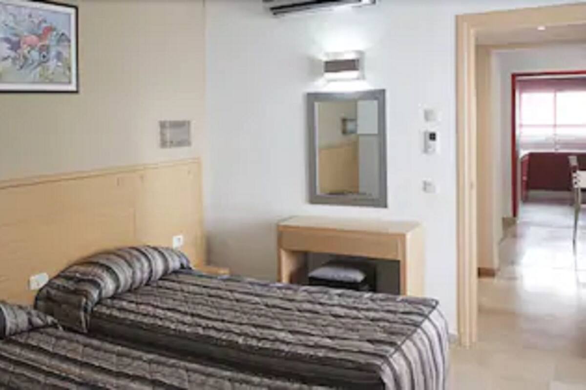 A hotel room with a bed, a small bedside table, a mirror, and a door leading to another room.
