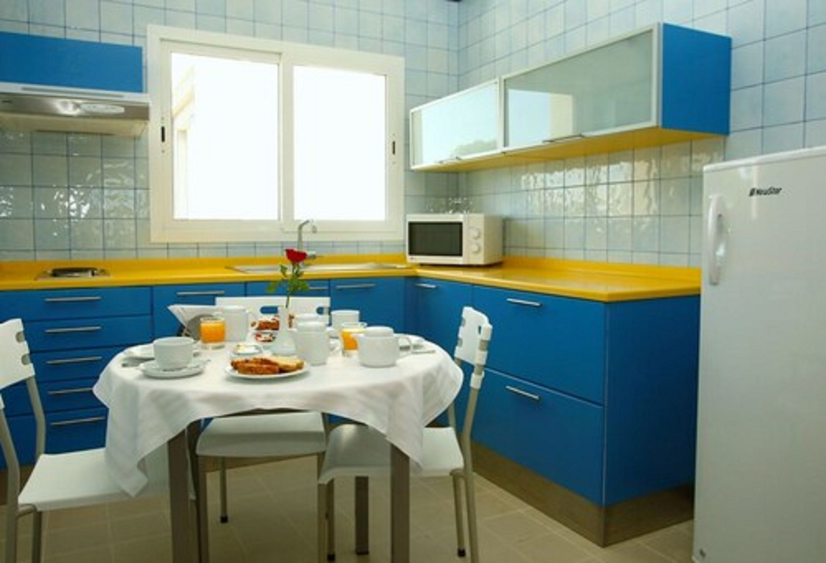 A kitchen with blue cabinets, a white refrigerator, and a dining table set for breakfast.