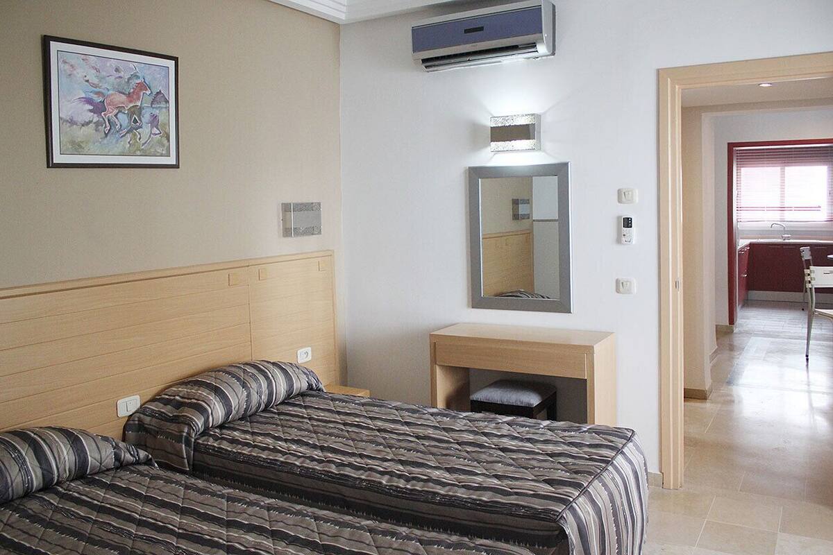 A hotel room with a bed, a bedside table, a mirror, and a painting on the wall.