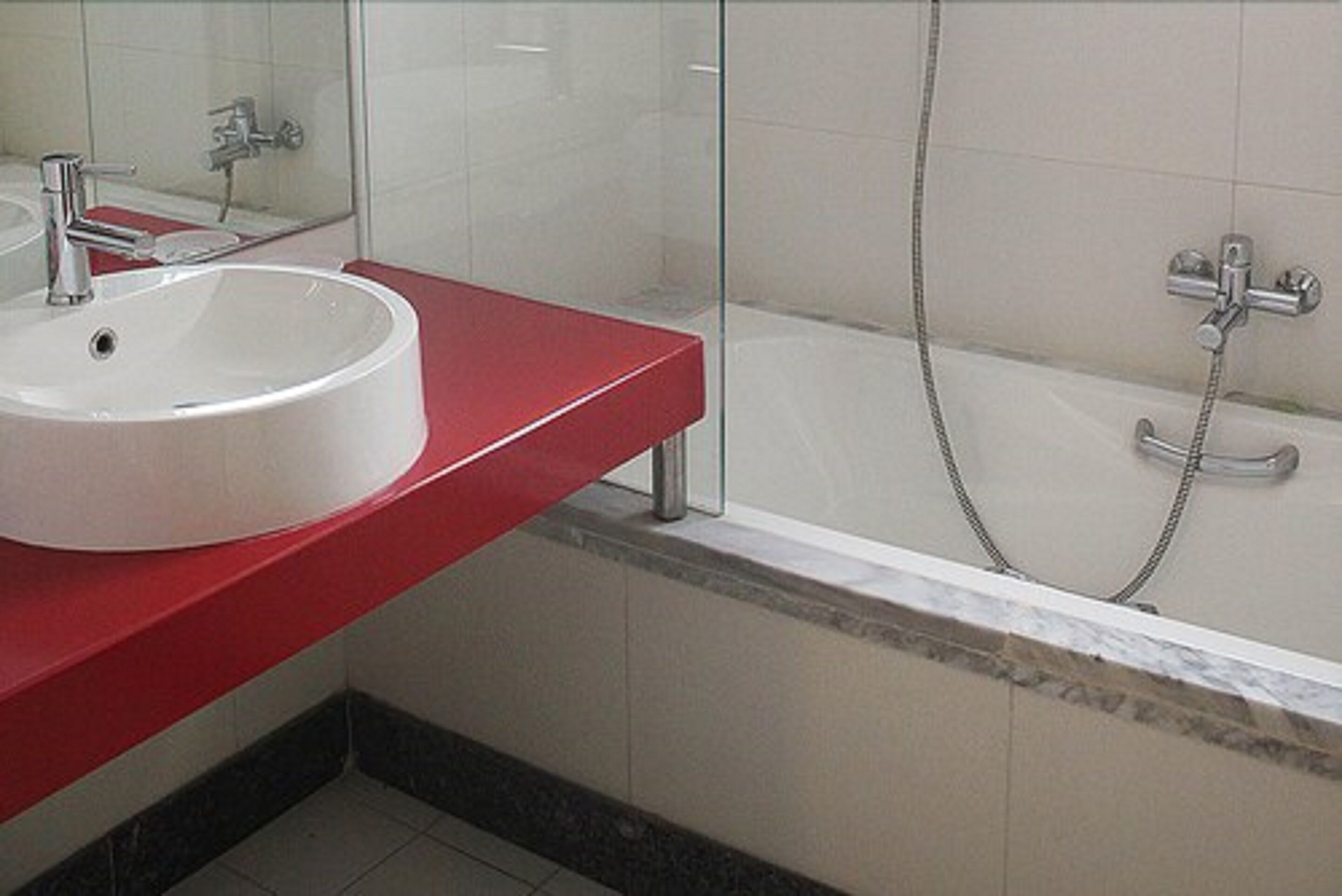 A bathroom with a white sink, red countertop, and a bathtub with a showerhead.