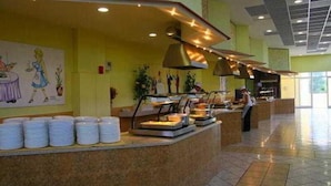 A buffet area with multiple food stations, a counter with stacked white containers, and a person serving.