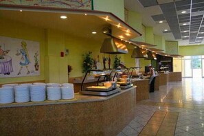 A buffet area with multiple food stations, a counter with stacked white containers, and a person serving. - Aqua Sun Village (Hersonissos)