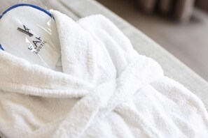 A white bathrobe with a logo and text on it, placed on a bed.