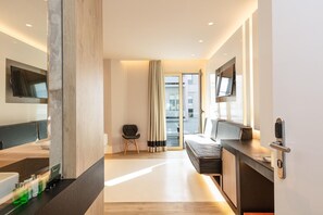 A modern hotel room with a bed, a desk, a chair, a television, and a sliding door to a balcony. - Kahlua Boutique Hotel (Hersonissos)