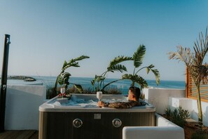 A hot tub with a person relaxing, surrounded by tropical plants, overlooking a body of water. - Kahlua Boutique Hotel (Hersonissos)