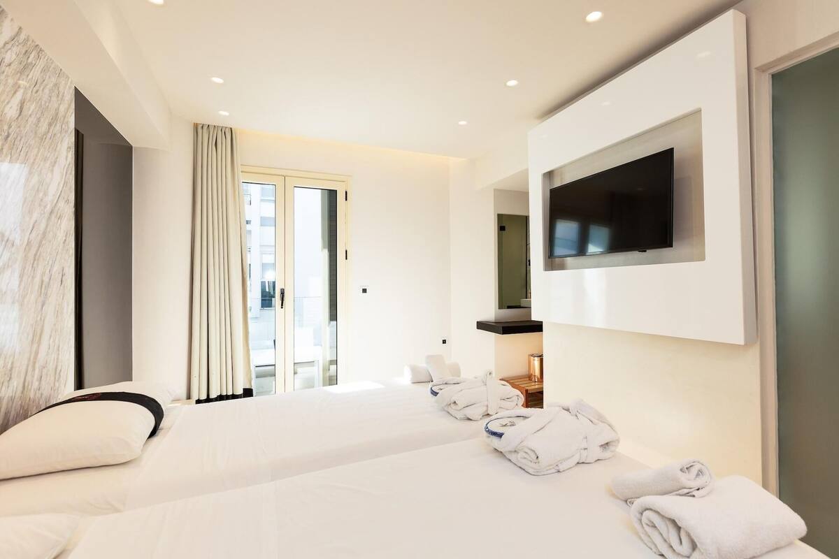 A hotel room with a bed, a TV mounted on the wall, and a view of the outside through a door.
